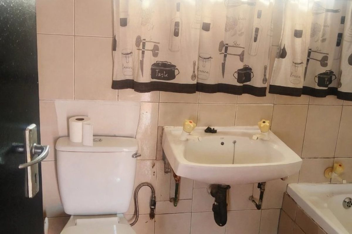 A dated bathroom featuring a wall-mounted basin, toilet, and bathtub with ceramic tiling throughout, requiring cosmetic updates to improve the overall aesthetic.