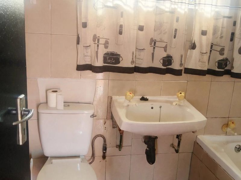 A dated bathroom featuring a wall-mounted basin, toilet, and bathtub with ceramic tiling throughout, requiring cosmetic updates to improve the overall aesthetic.