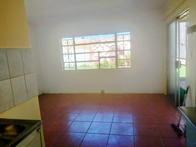 An empty open-plan living and kitchen area featuring tiled flooring, a sliding glass door, and security window bars, awaiting modernization.