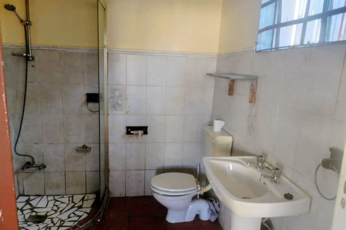 A dated bathroom featuring a shower enclosure, pedestal basin, and toilet, with tiled finishes throughout. The space requires cosmetic updates and modernization.