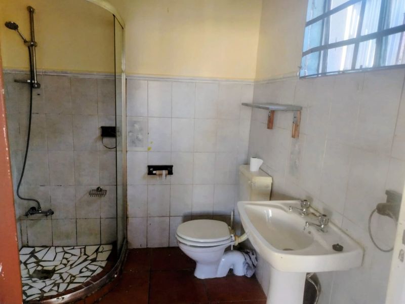 A dated bathroom featuring a shower enclosure, pedestal basin, and toilet, with tiled finishes throughout. The space requires cosmetic updates and modernization.