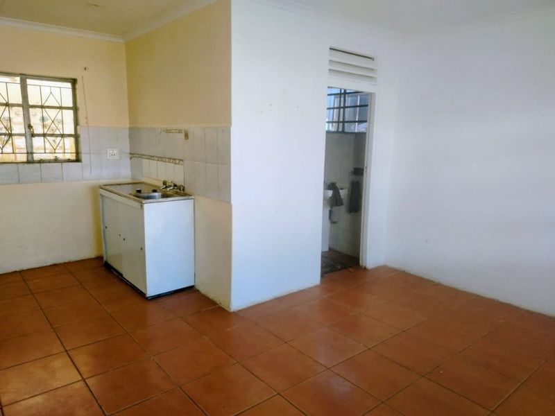 A basic, empty kitchen area featuring tiled flooring, a simple sink unit, and tiled splashbacks, offering a blank canvas for potential renovation.