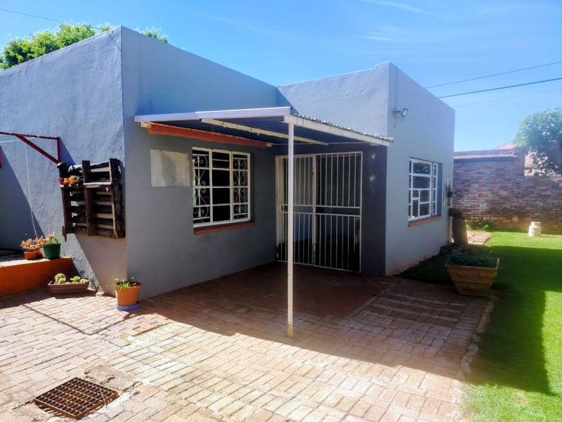 Rear exterior view of the apartment featuring a brick-paved patio area, covered awning, and secure metal window and door fixtures.