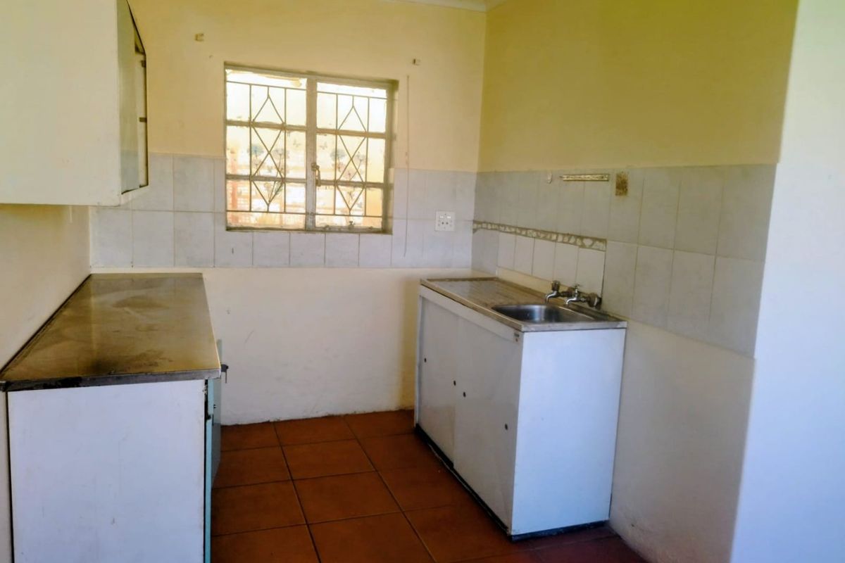 A functional, empty kitchen featuring tiled flooring, a stainless steel sink, and basic cabinetry, offering a blank canvas for potential renovation and modernization.