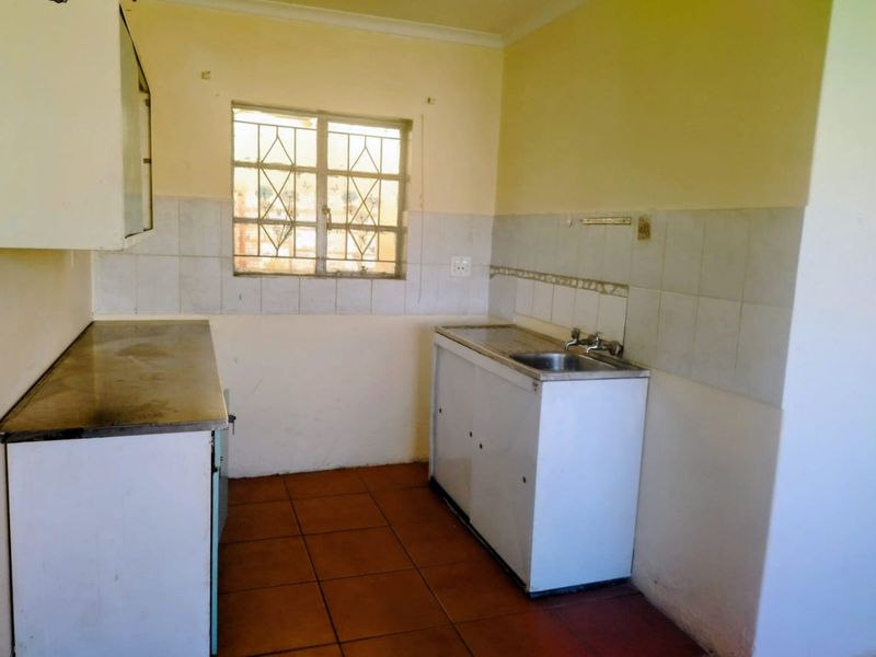 A functional, empty kitchen featuring tiled flooring, a stainless steel sink, and basic cabinetry, offering a blank canvas for potential renovation and modernization.