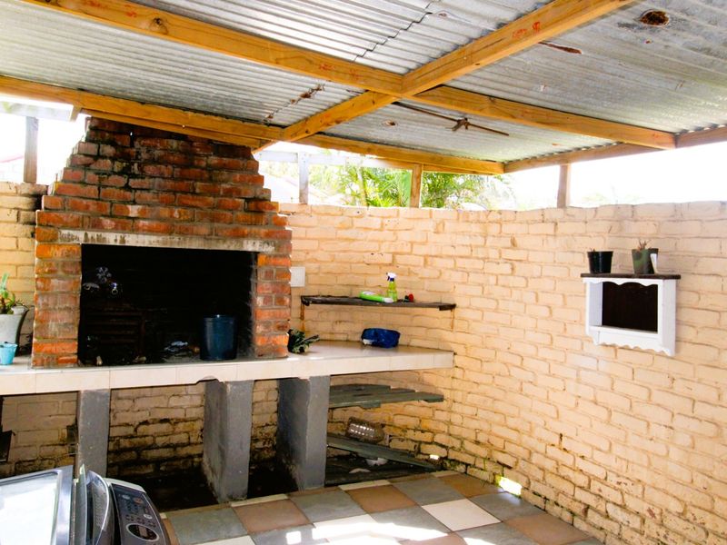 Covered outdoor patio area featuring a built-in brick braai, concrete prep surface, and exposed brick walls under a corrugated iron roof.