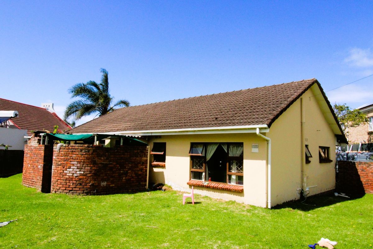 Rear view of the house featuring a tiled roof, brick boundary wall, and lawn area, showing signs of exterior wear.