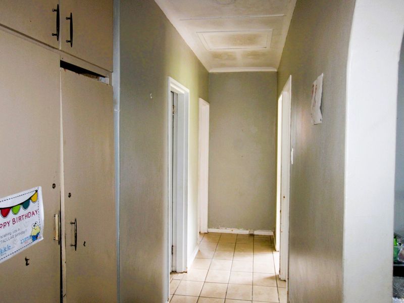 A functional hallway featuring built-in storage cupboards, tiled flooring, and an arched entryway, showing signs of wear and ceiling water damage.