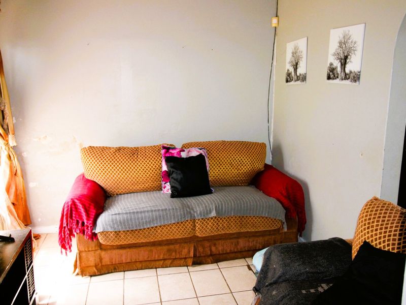 A living room area featuring tiled flooring and neutral wall finishes, currently showing signs of wear and surface damage.