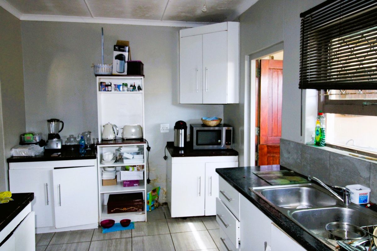 A functional kitchen featuring white cabinetry, dark granite countertops, and a double stainless steel sink, showing signs of wear and moisture damage.