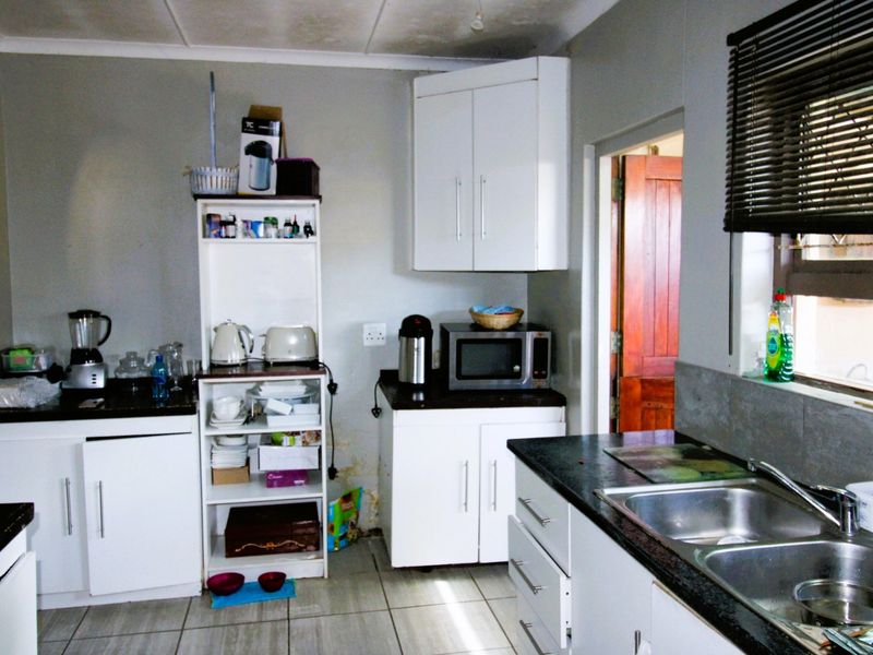 A functional kitchen featuring white cabinetry, dark granite countertops, and a double stainless steel sink, showing signs of wear and moisture damage.