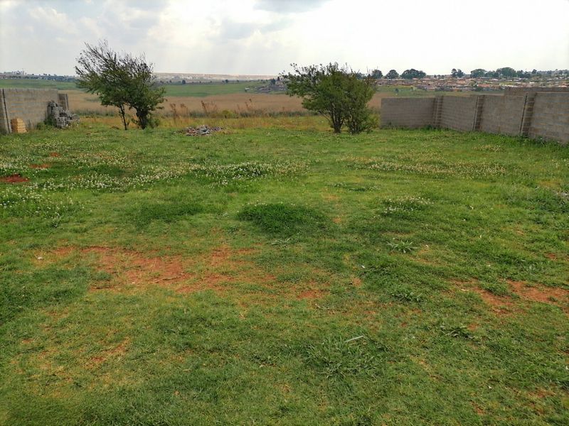 A spacious, undeveloped garden area featuring a grass lawn and partial perimeter boundary walls with open views of the surrounding landscape.