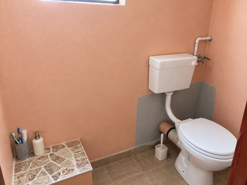 A small bathroom featuring a standard toilet with exposed plumbing and a tiled vanity surface, requiring cosmetic updates to the wall finishes.