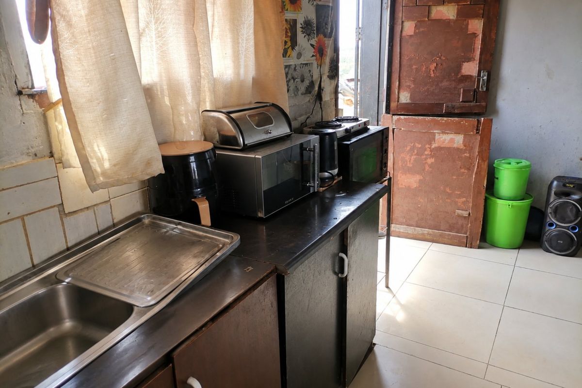 A functional kitchen area featuring a stainless steel double sink, laminate countertops, and tiled flooring, requiring cosmetic updates to the cabinetry and door.