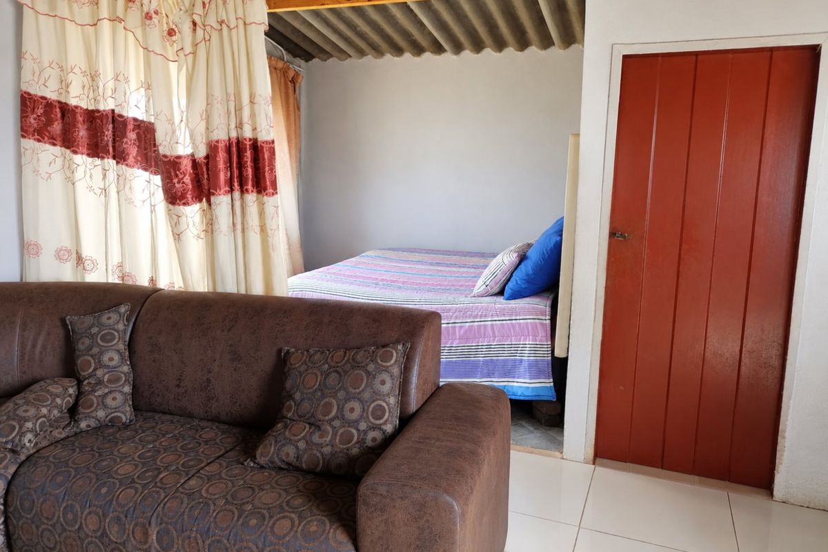 A bedroom featuring exposed timber rafters, corrugated roof sheeting, and tiled flooring, with a solid timber door providing access.