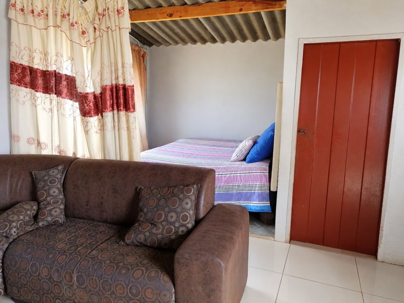 A bedroom featuring exposed timber rafters, corrugated roof sheeting, and tiled flooring, with a solid timber door providing access.