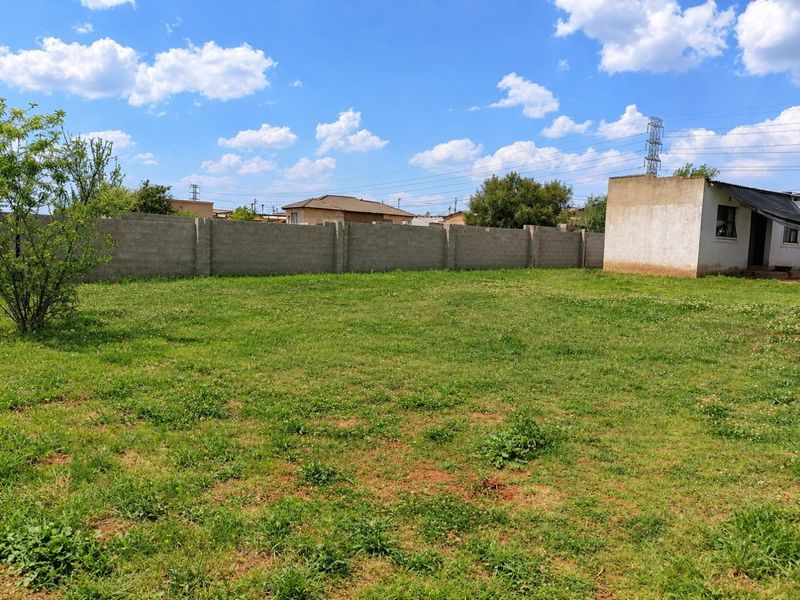A spacious backyard featuring a large grass lawn enclosed by a concrete perimeter wall, adjacent to the main dwelling structure.