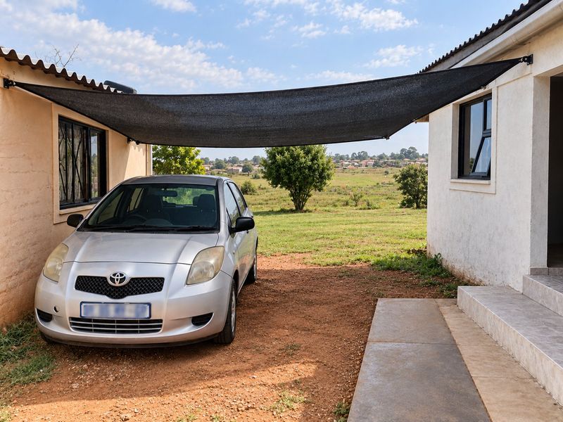 Rear exterior area featuring a shade sail, tiled entrance steps, and aluminium window frames, overlooking an open field.