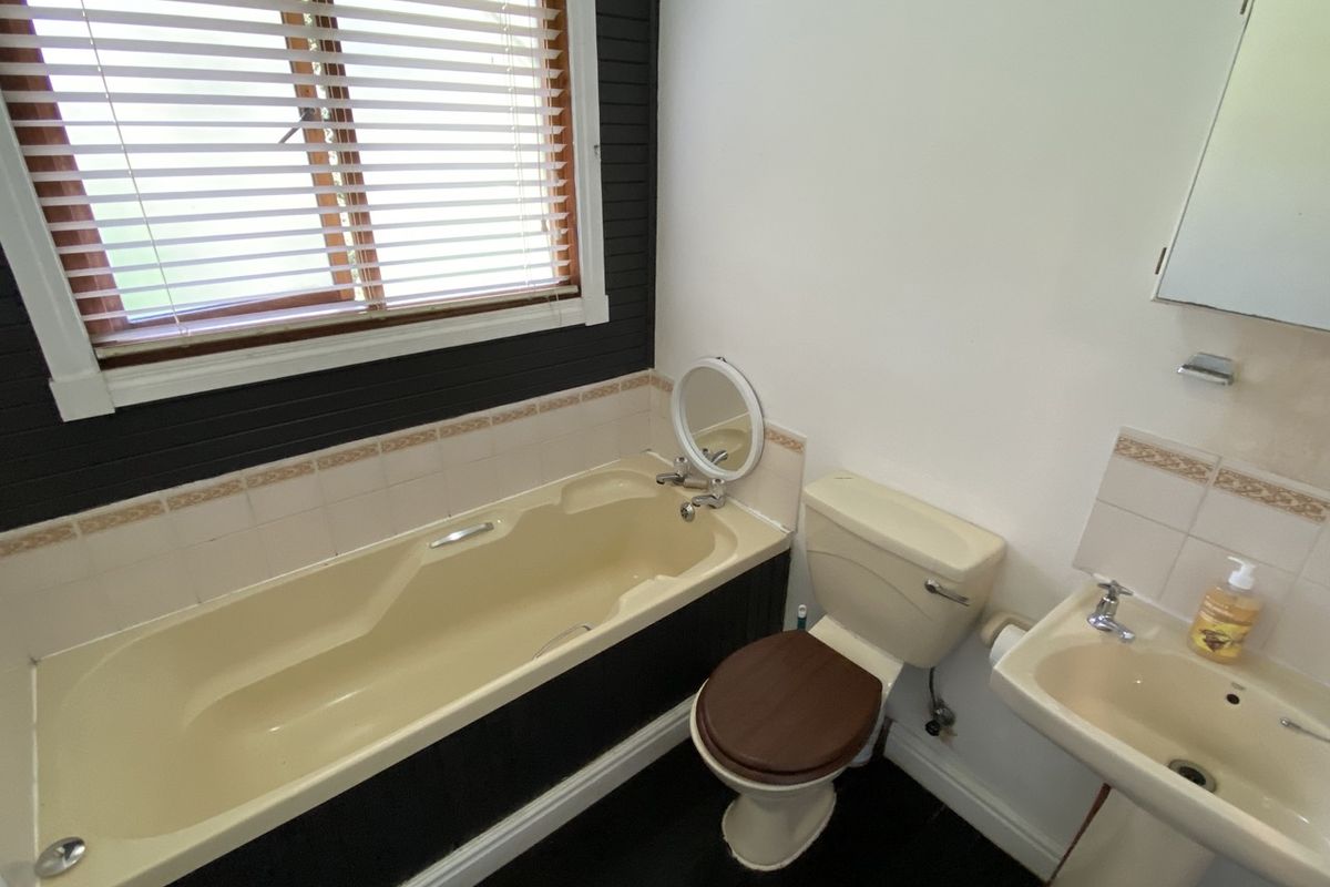 A functional bathroom featuring a bathtub, pedestal sink, and toilet, with a tiled splashback and window blinds.