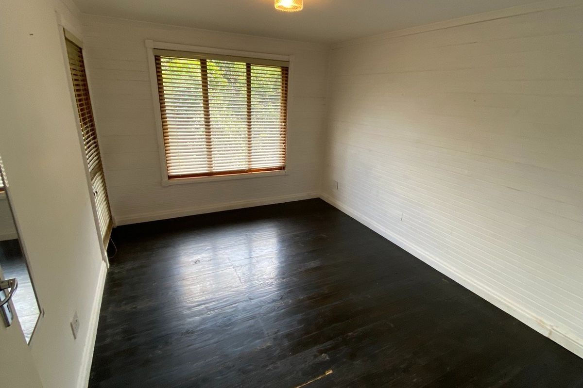 An empty bedroom featuring dark stained timber flooring, white timber wall paneling, and venetian blinds.