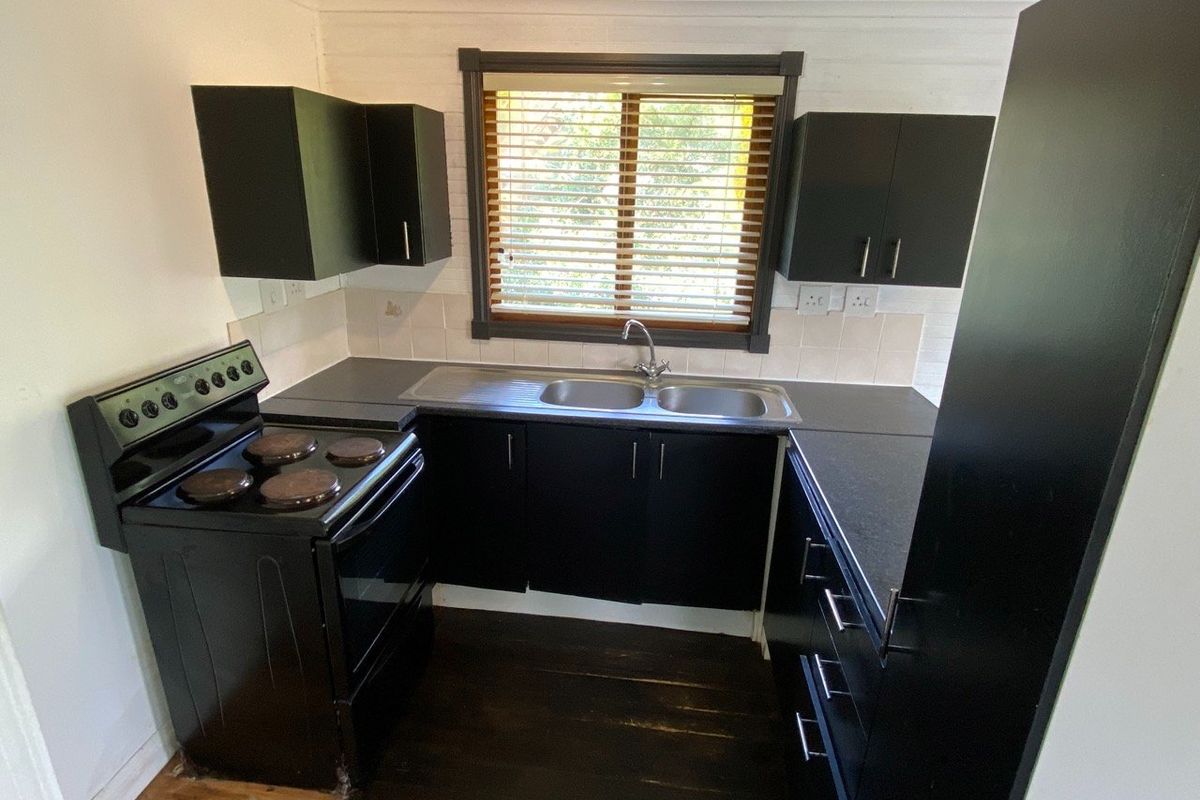 Compact kitchen featuring black cabinetry, double bowl sink, tiled backsplash, and a freestanding electric stove with natural light from the window.