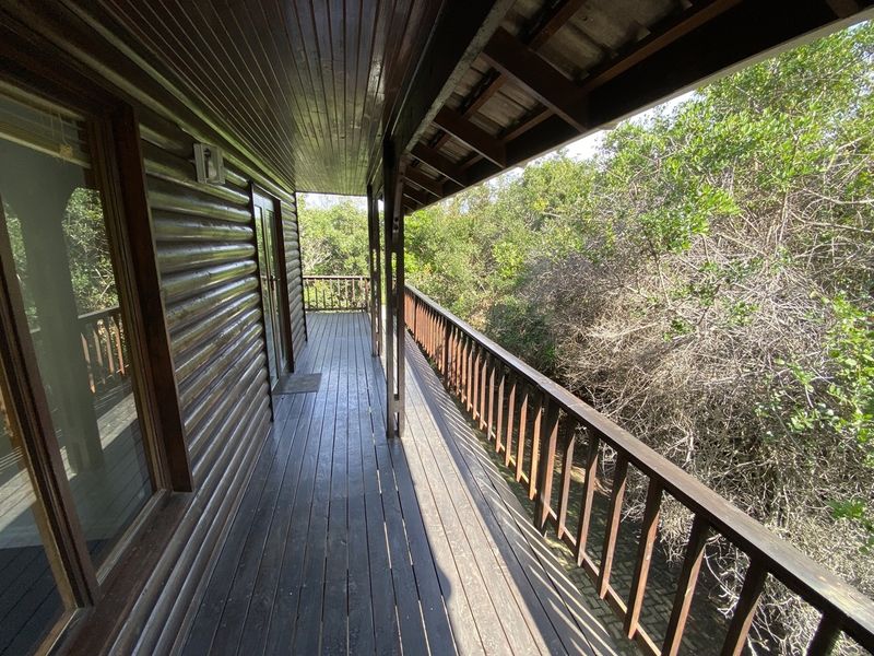 A covered timber balcony featuring wooden decking and balustrades, overlooking dense surrounding vegetation.