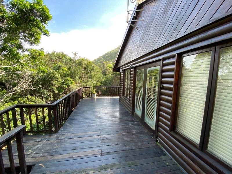 A spacious wooden balcony deck attached to a log cabin style home, featuring a timber balustrade and views of the surrounding natural landscape.