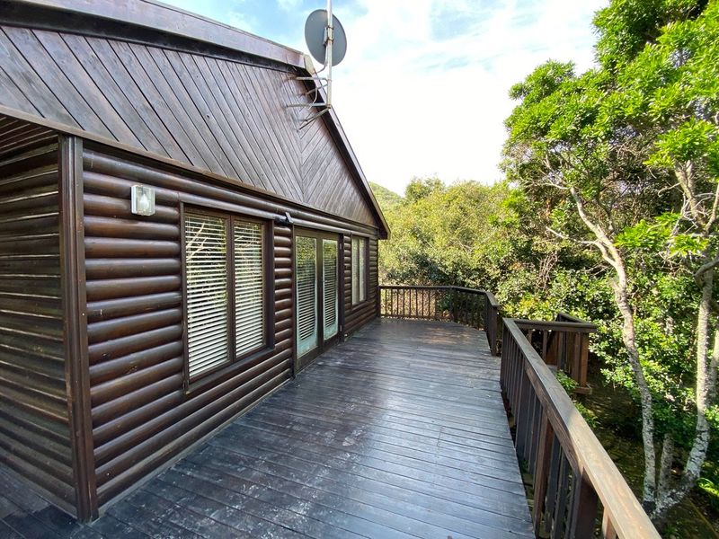 A spacious wooden balcony deck attached to a log cabin style home, featuring timber railings and views of the surrounding trees.