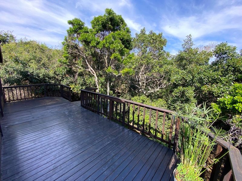 A spacious elevated timber deck featuring a wooden balustrade, offering a peaceful outlook over the surrounding mature trees and natural greenery.