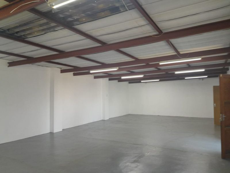 A spacious, empty commercial utility area featuring exposed steel beams, fluorescent lighting, and a clean painted concrete floor.