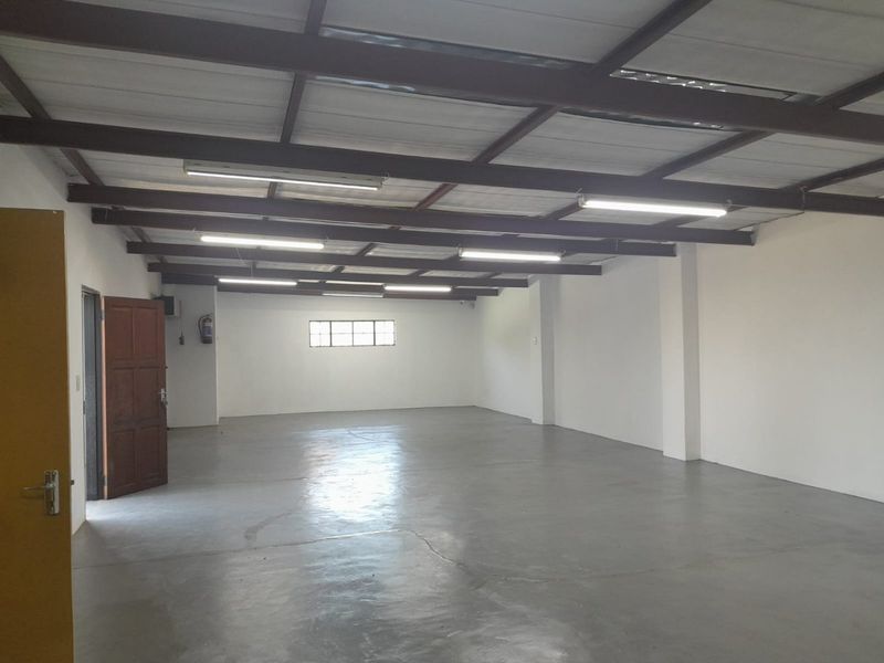 A spacious, empty commercial utility area featuring exposed steel roof trusses, fluorescent lighting, and durable concrete flooring.