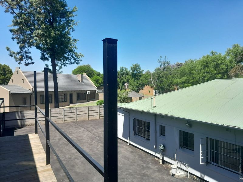 Elevated timber balcony overlooking a paved commercial courtyard with security-fitted buildings and mature trees.