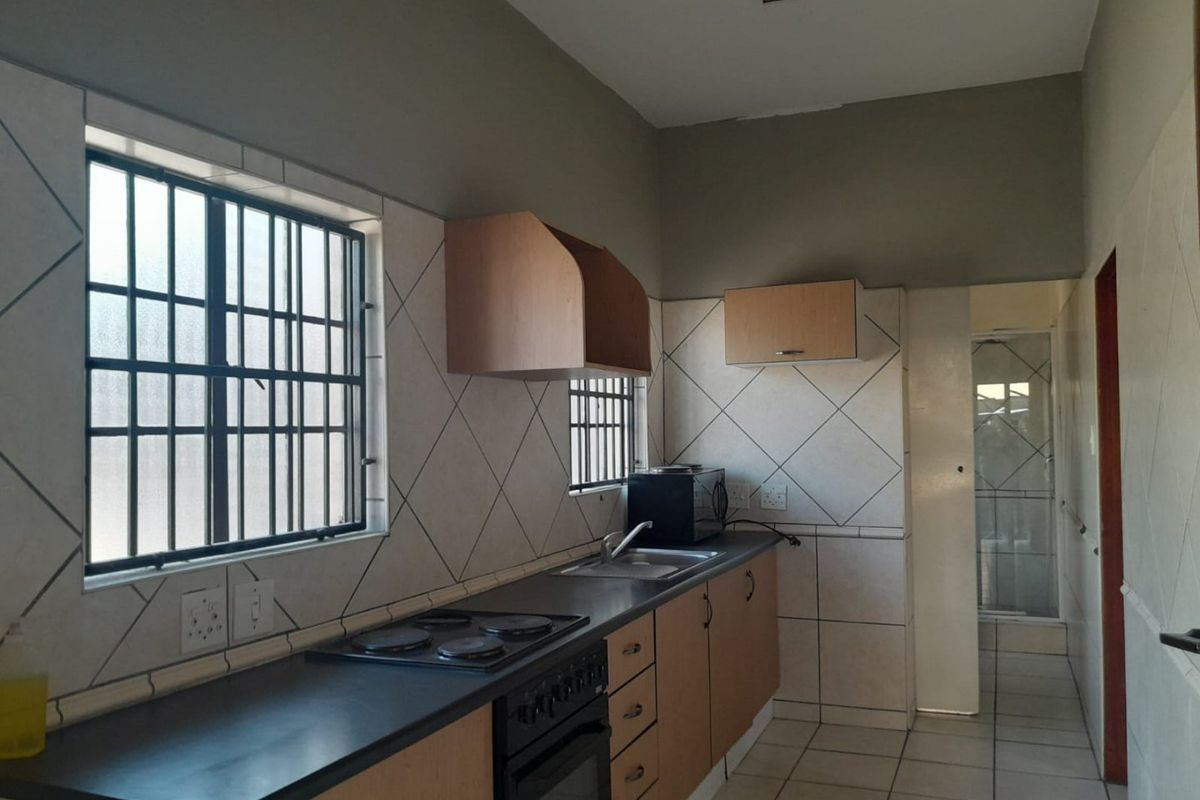 Functional kitchen featuring built-in cabinetry, laminate countertops, an integrated electric stove and oven, tiled backsplash, and tiled flooring with security bars on windows.
