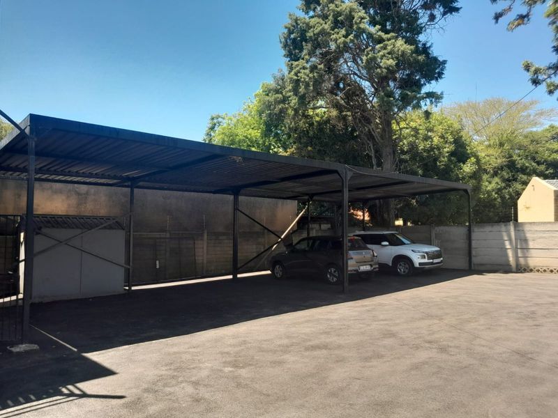 Covered parking area featuring a metal carport structure, asphalt paving, and perimeter walling with electric fencing.