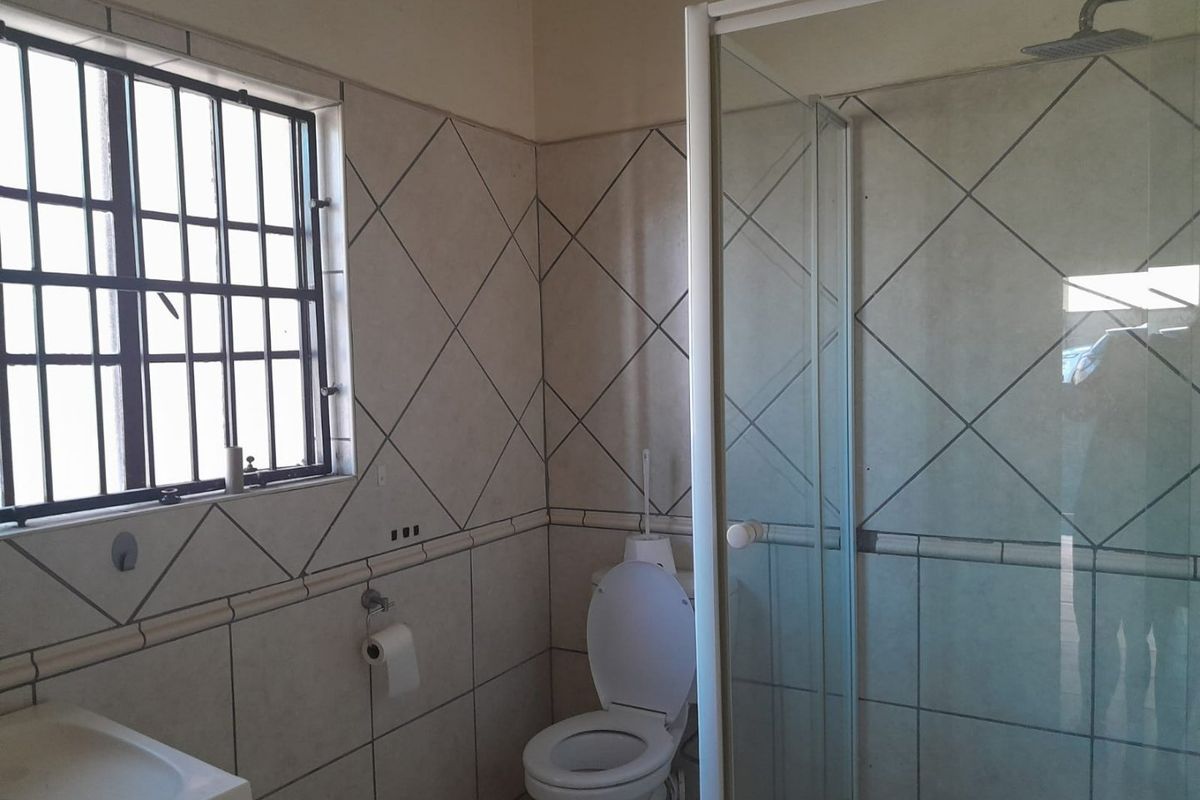 A functional bathroom featuring a shower enclosure, toilet, and wash basin with tiled walls and security bars on the window.