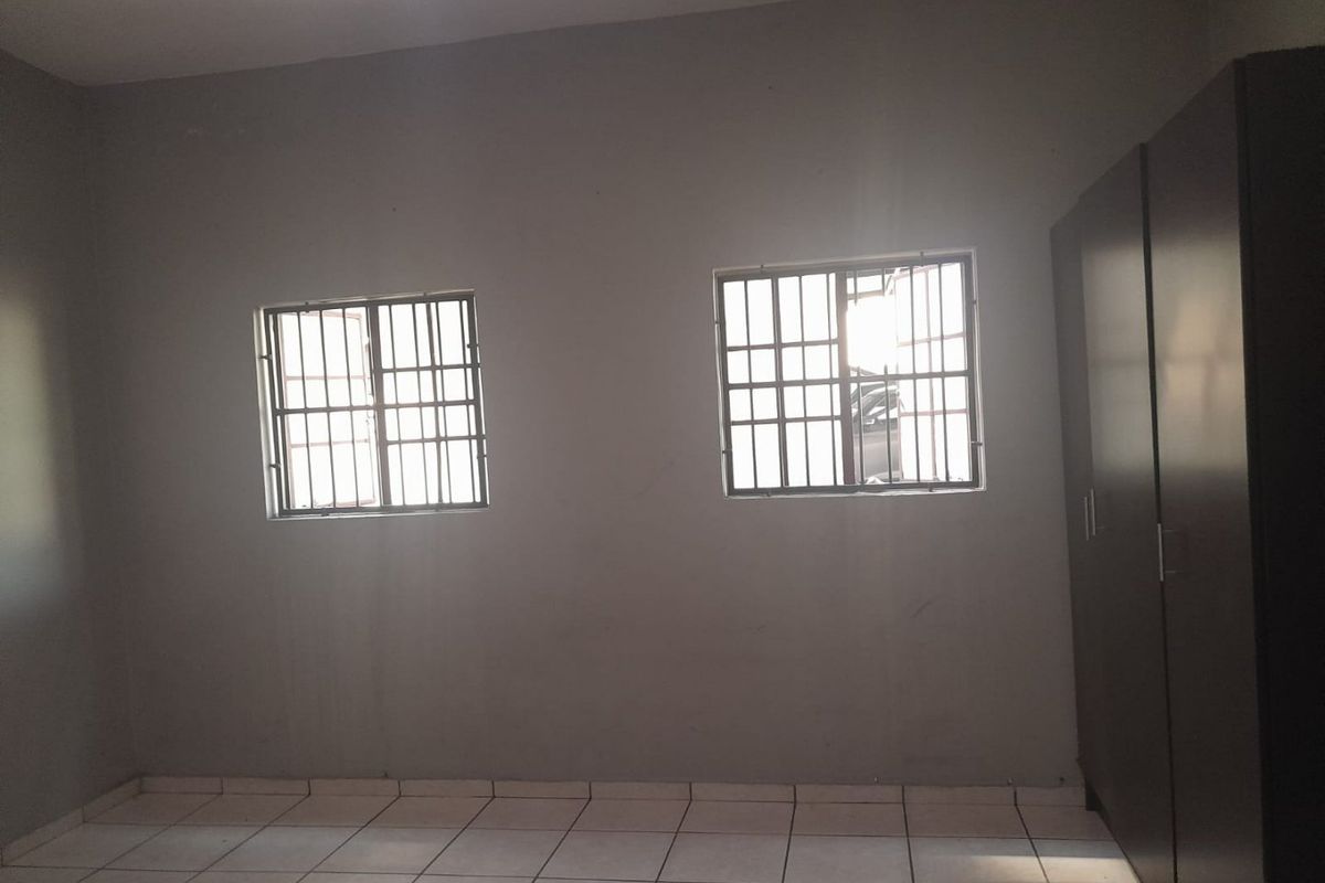 A bedroom featuring tiled flooring, built-in wardrobe storage, and windows fitted with security bars.