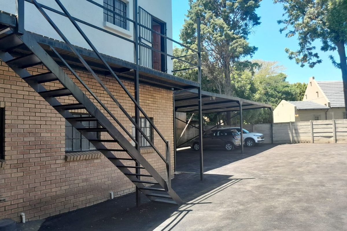 Rear exterior view of the commercial property featuring a metal staircase, covered carport parking, and paved driveway area.