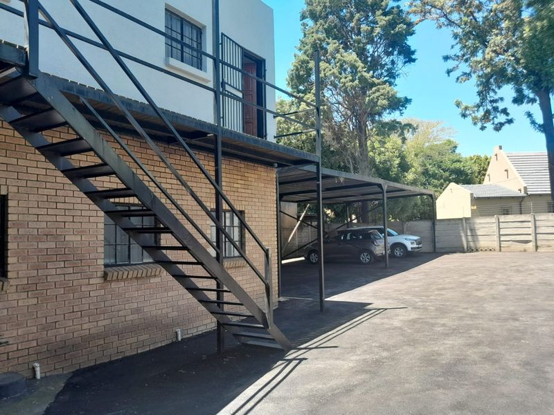 Rear exterior view of the commercial property featuring a metal staircase, covered carport parking, and paved driveway area.