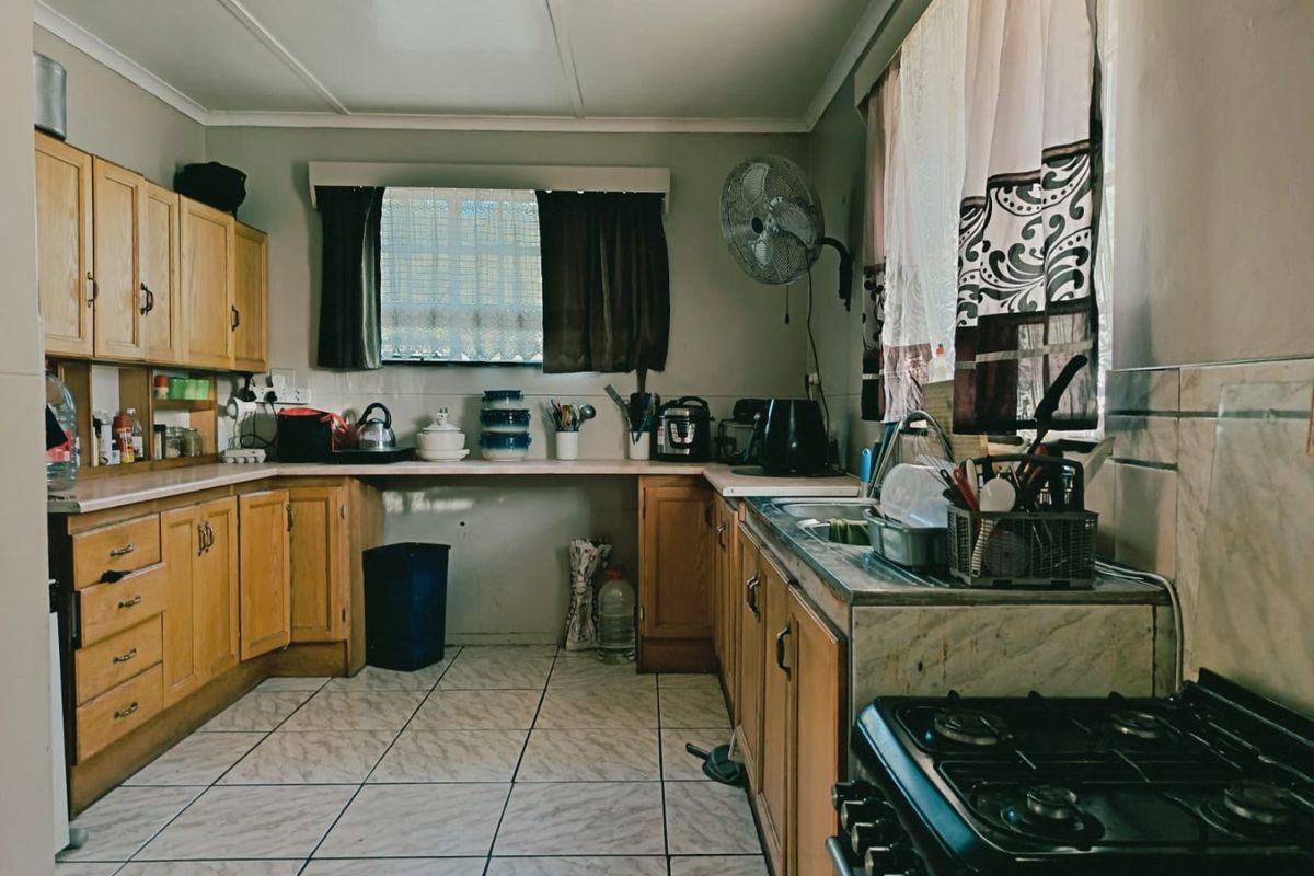 A functional kitchen featuring wooden cabinetry, laminate countertops, tiled flooring, and a stainless steel sink, offering a traditional layout with ample storage space.