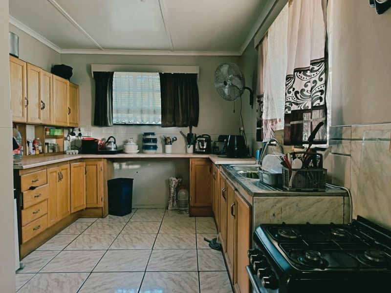 A functional kitchen featuring wooden cabinetry, laminate countertops, tiled flooring, and a stainless steel sink, offering a traditional layout with ample storage space.