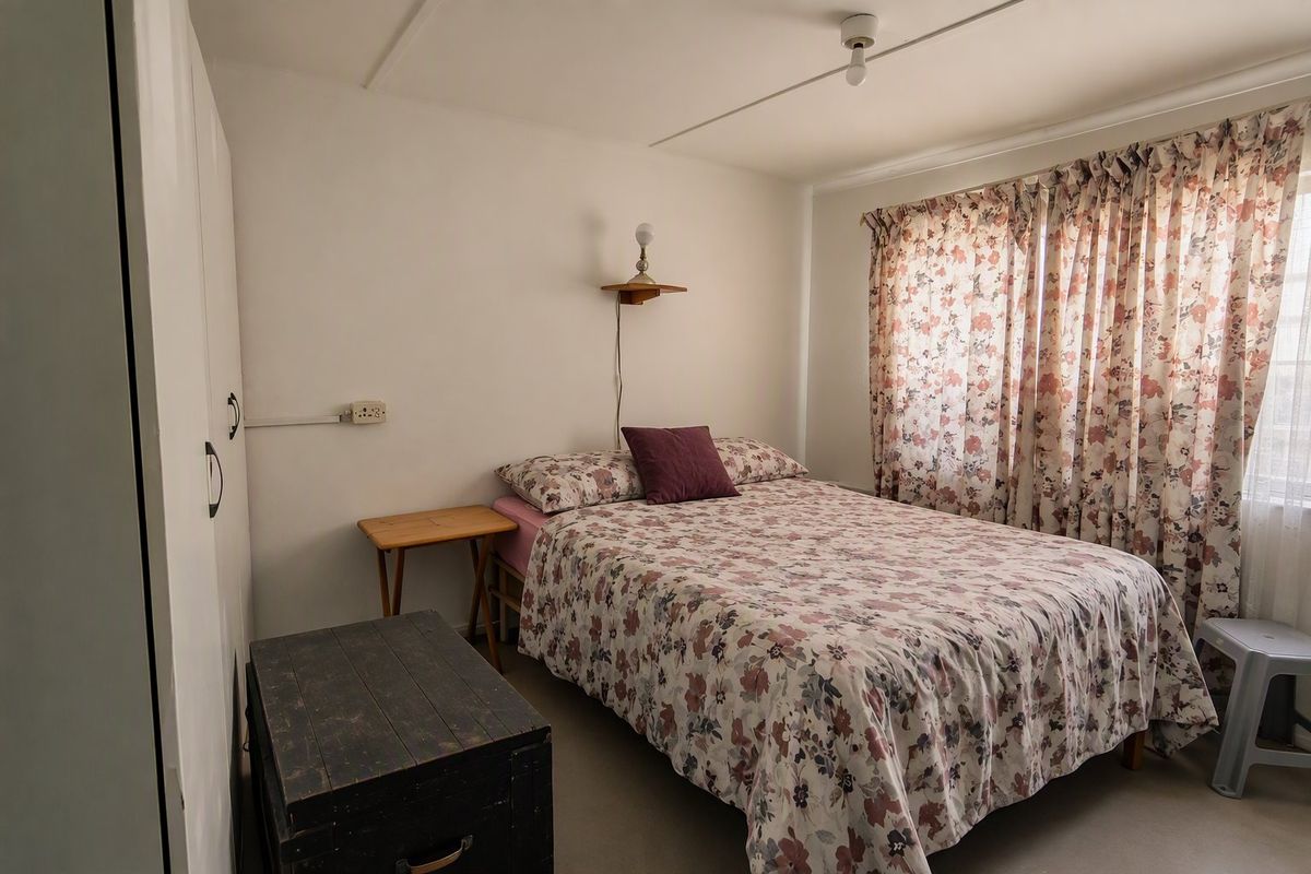 A functional bedroom featuring built-in wardrobe storage and a wall-mounted light fixture, offering a neutral base for potential interior updates.