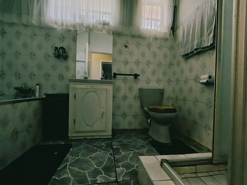 A dated bathroom featuring a built-in vanity, bathtub, and toilet with original wall and floor tiling, offering significant potential for modernization.