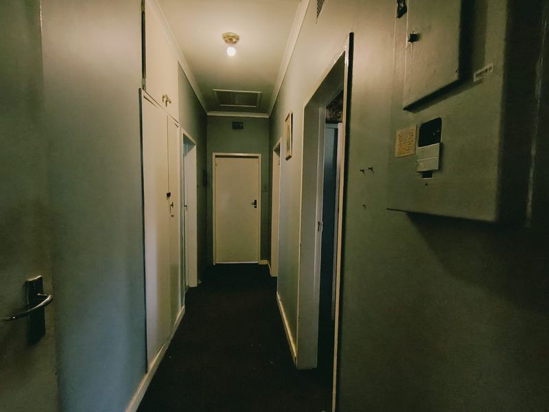 A functional hallway featuring built-in storage cupboards and a wall-mounted electrical distribution board, providing access to multiple rooms within the home.