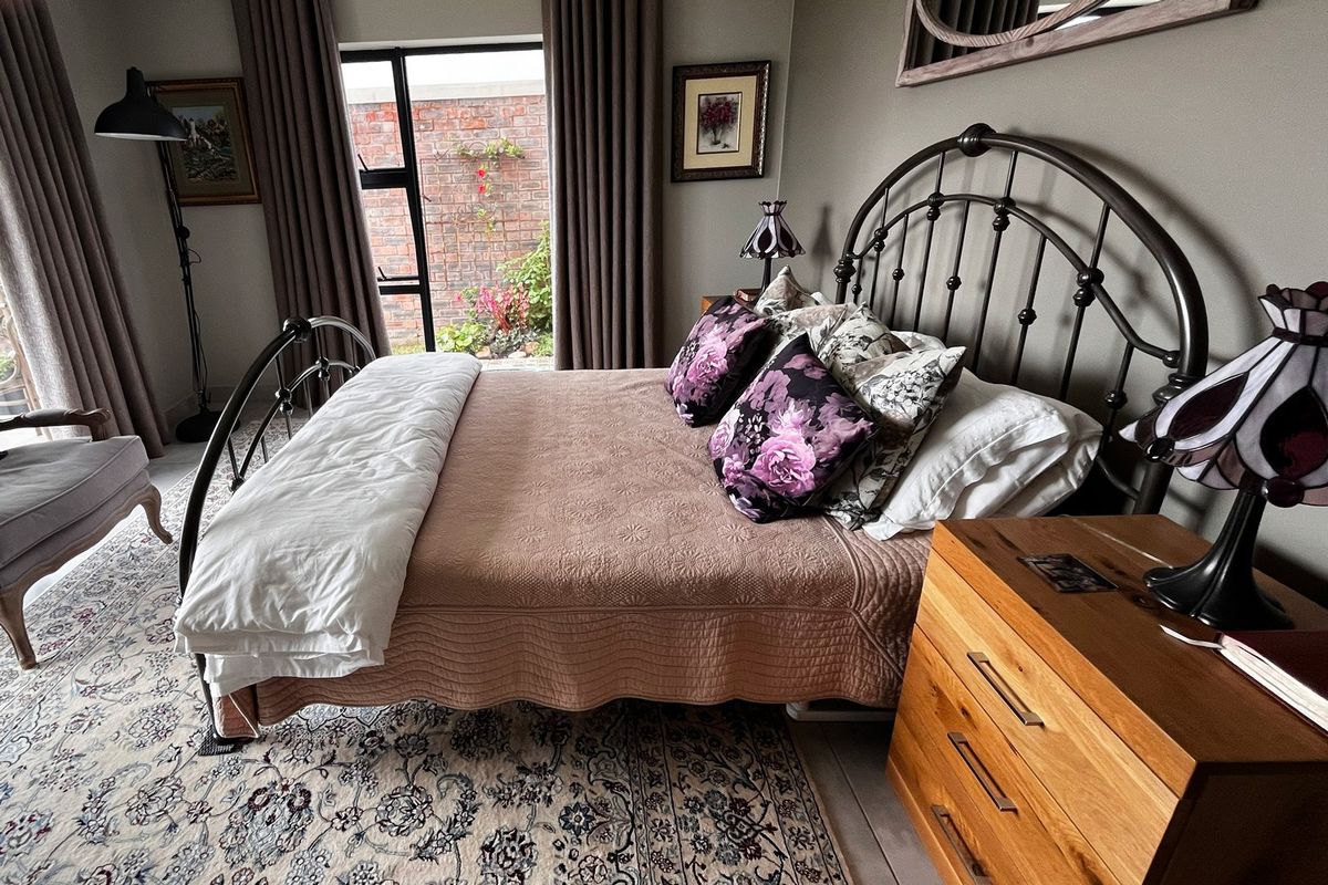 A well-maintained bedroom featuring tiled flooring and large aluminium-framed windows that provide natural light and a view of the private rear courtyard.