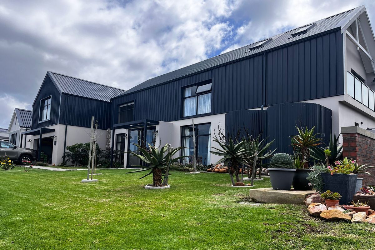 A modern architectural home featuring dark corrugated metal cladding, a pitched roof with skylights, and a well-maintained garden area.