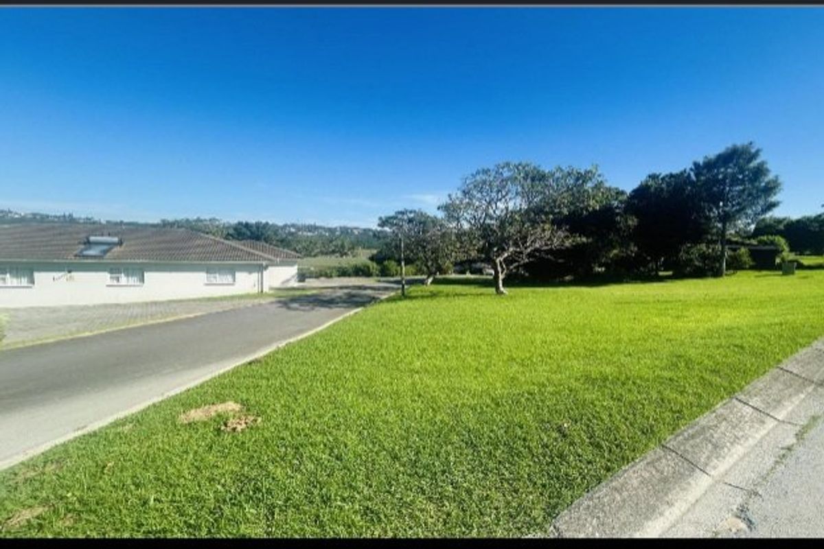 A view of the residential property frontage featuring a well-maintained lawn, mature trees, and a paved driveway leading to the adjacent dwelling.