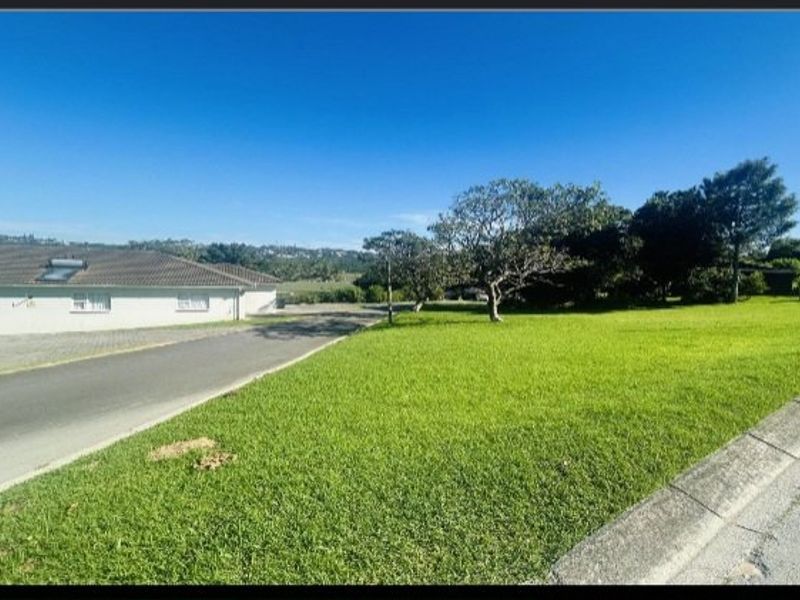A view of the residential property frontage featuring a well-maintained lawn, mature trees, and a paved driveway leading to the adjacent dwelling.