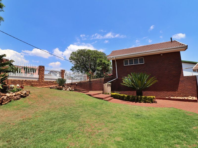 A well-maintained rear garden area featuring a brick exterior, paved pathways, retaining walls, and secure perimeter fencing.