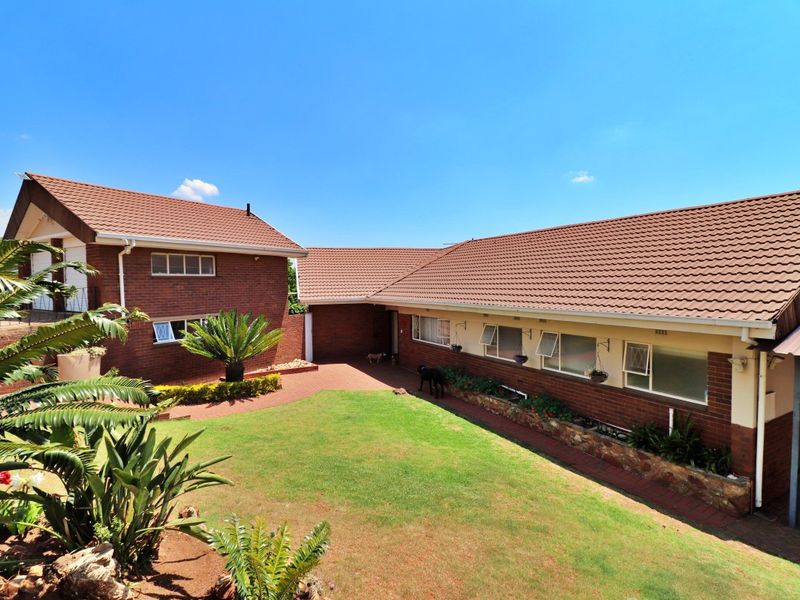 A well-maintained rear exterior view of a brick house featuring a tiled roof, paved courtyard, and a landscaped garden area.