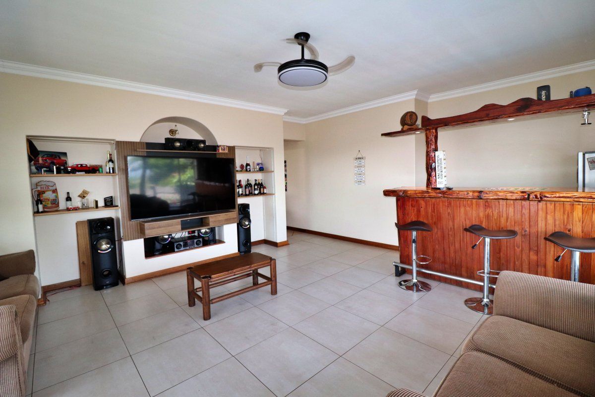 Spacious living room featuring tiled flooring, a built-in entertainment unit with shelving, and a rustic wooden bar counter.